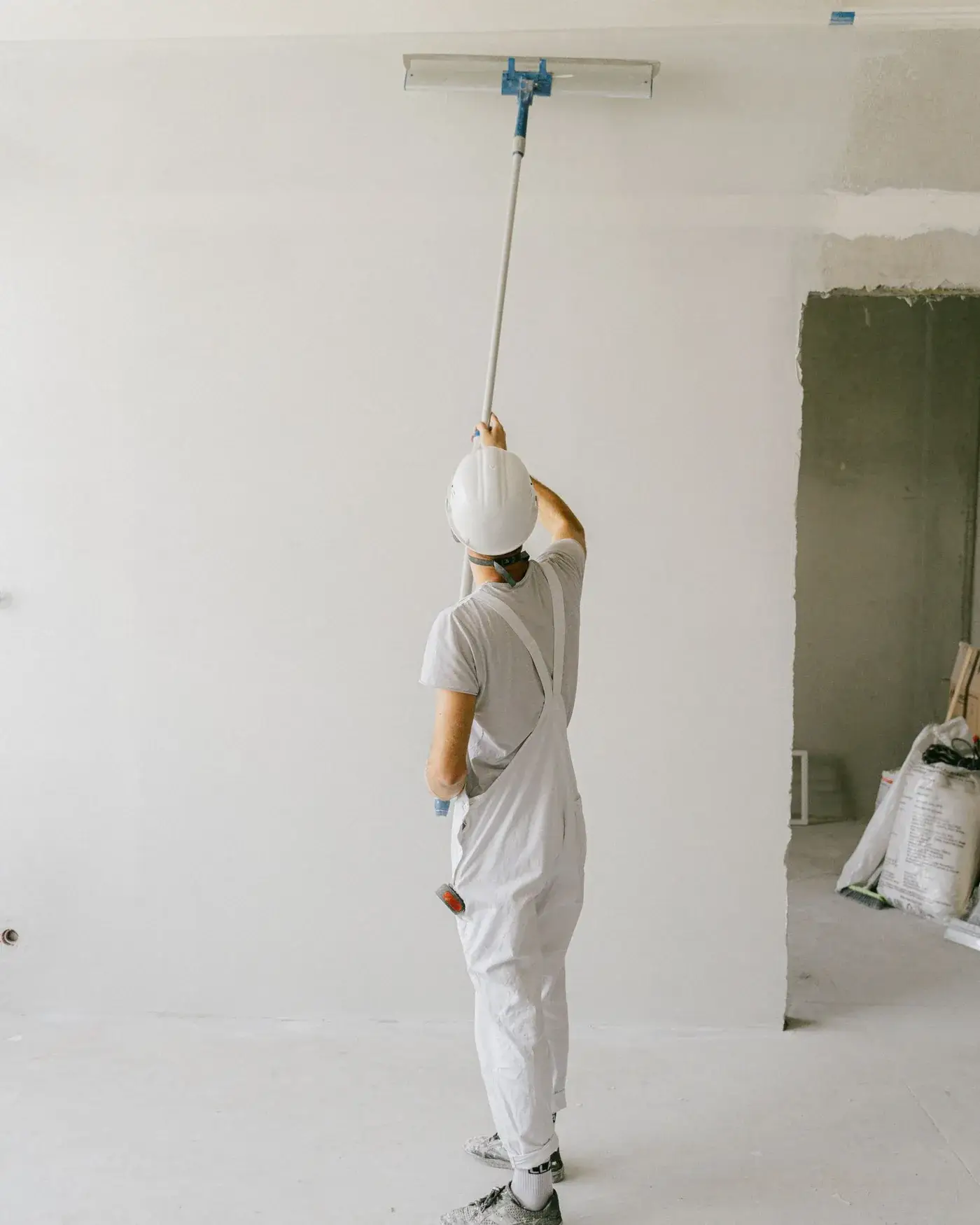Painter rolling an interior wall in white overalls